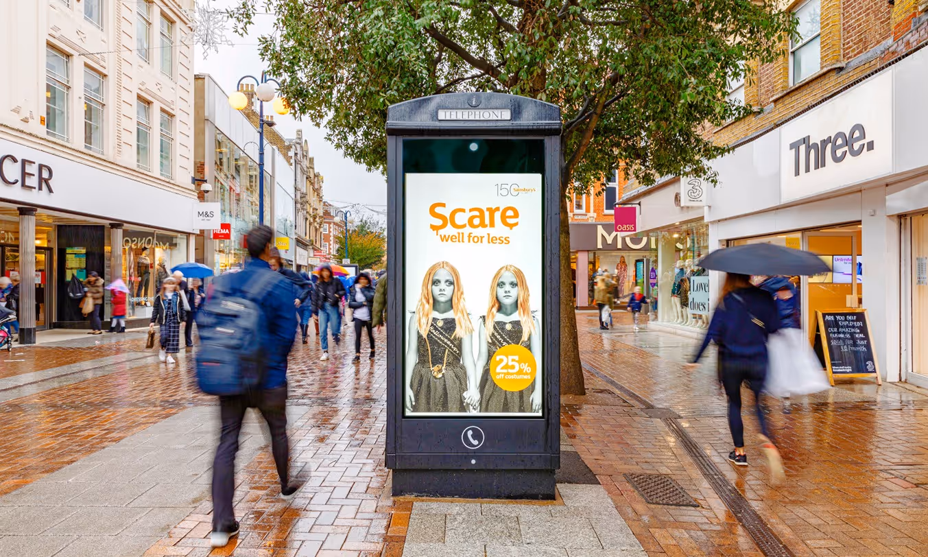 Sainsbury's Halloween advert on a digital screen on a New World Payphone on a busy street as buses and pedestrians pass by during the day