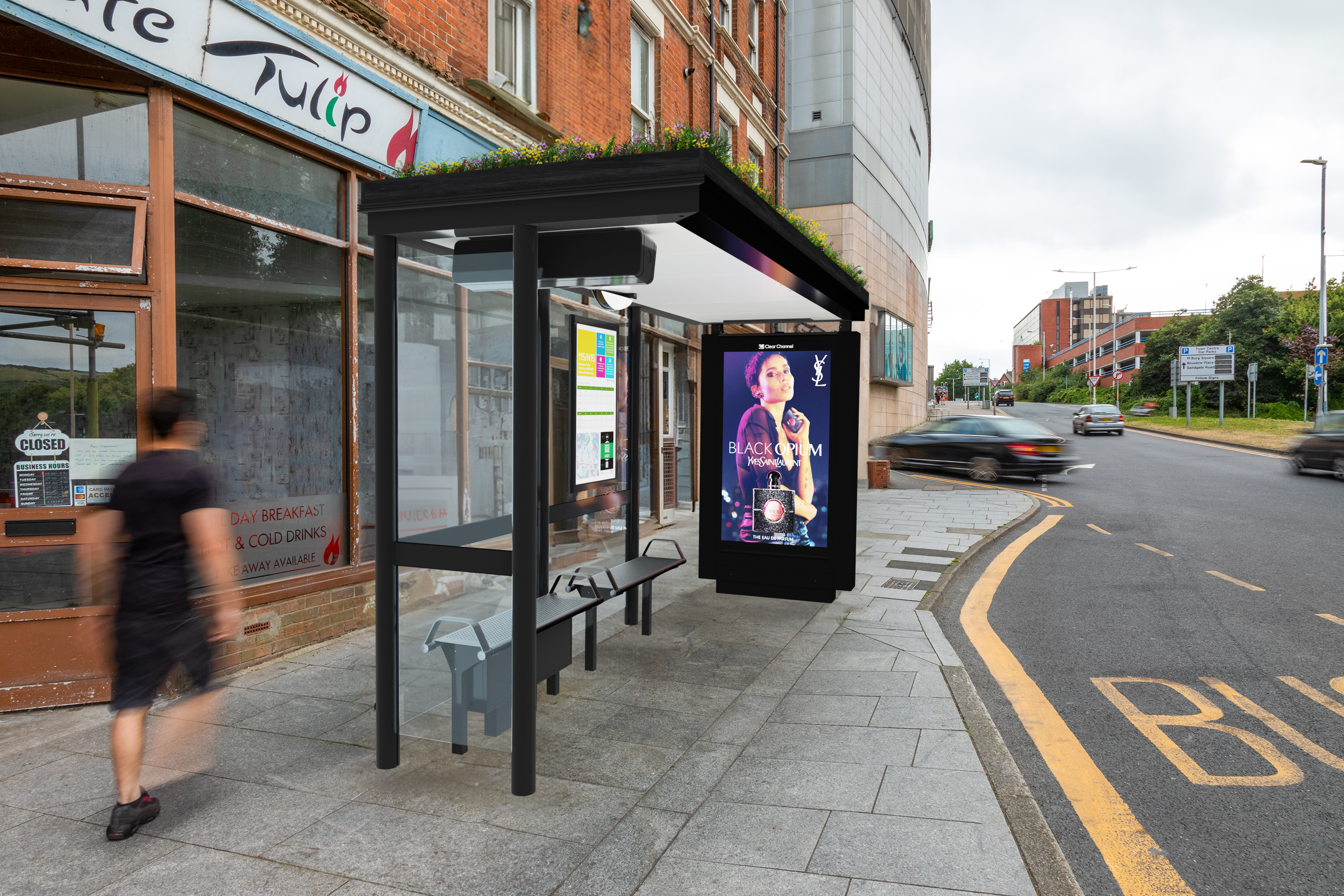 A bus shelter with a Living Roof on top sits on a sidewalk, during the day, as pedestrians and cars pass by