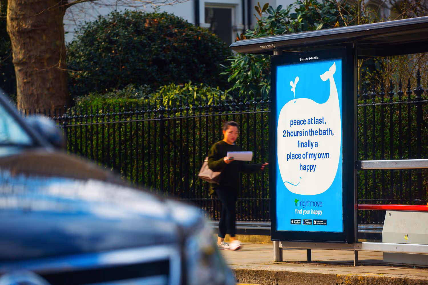 A bus stop poster with a woman walking by
