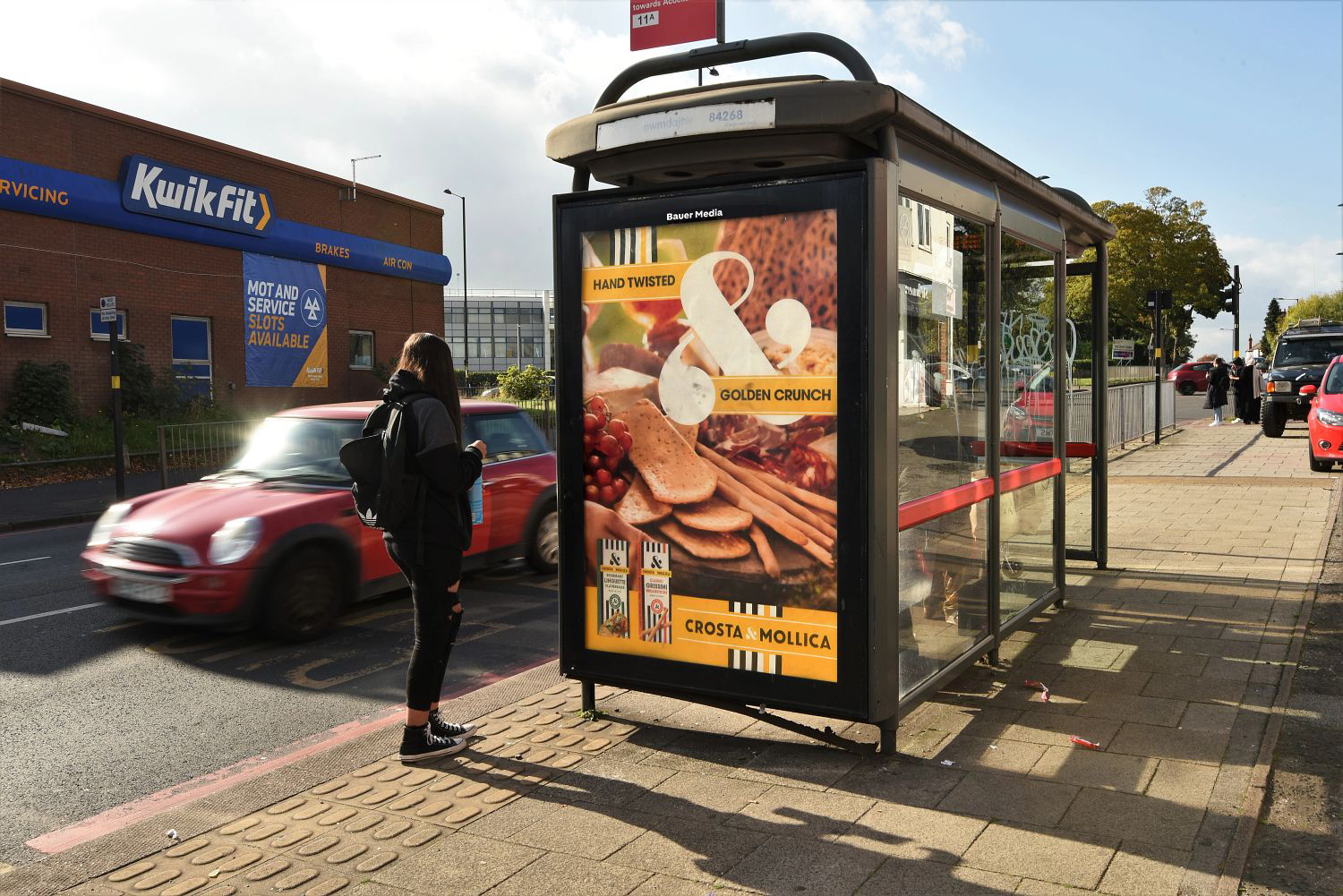 Crosta & Mollica advertising on a outdoor poster outside Kwik Fit with a person walking by