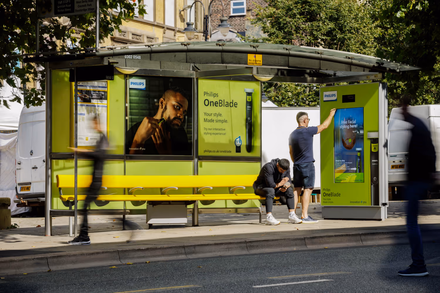 A full poster wrap by Philips OneBlade on a bus stop with someone interacting with the digital advert