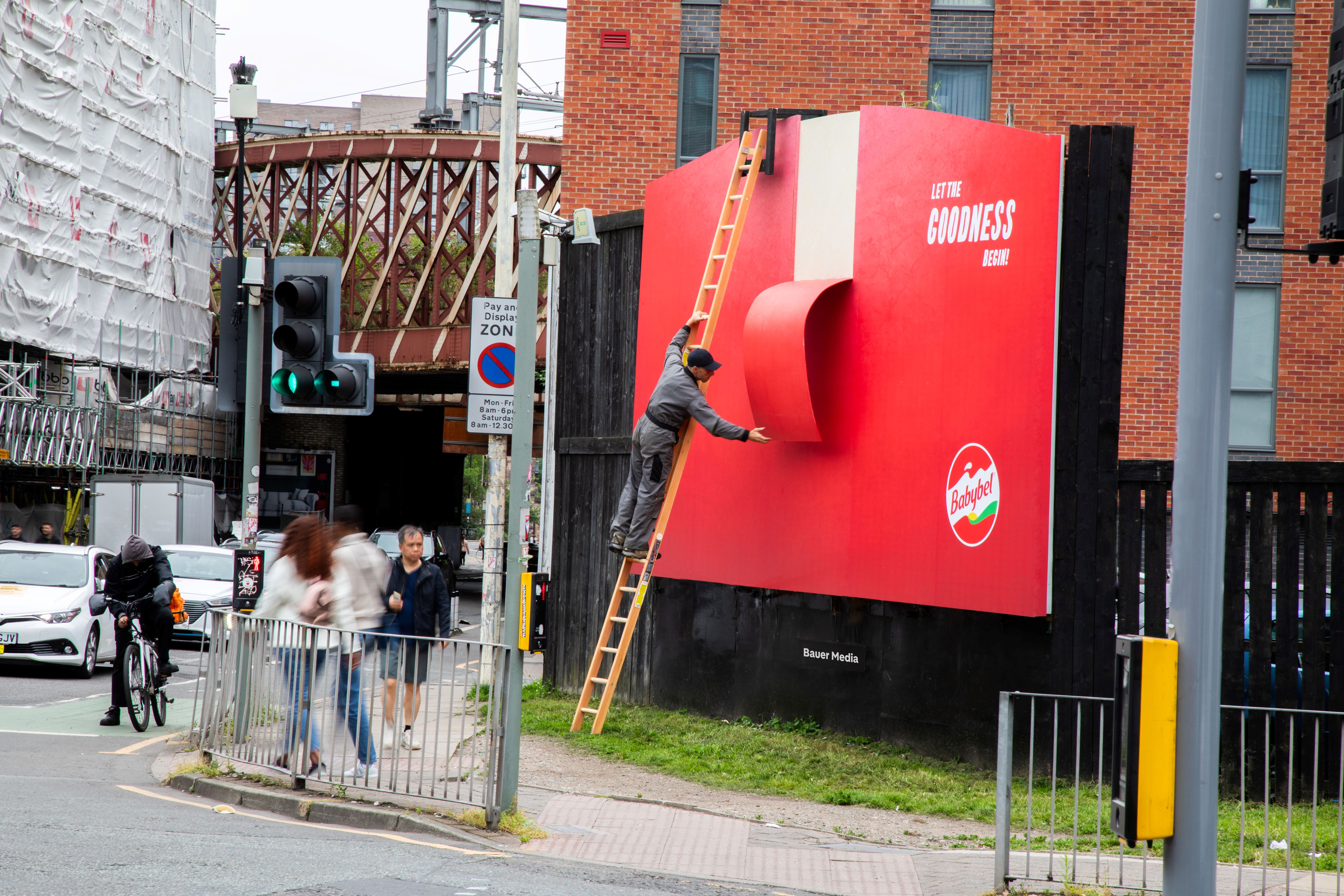 A special build Babybel ad on a street corner, during the day, as pedestrians pass by