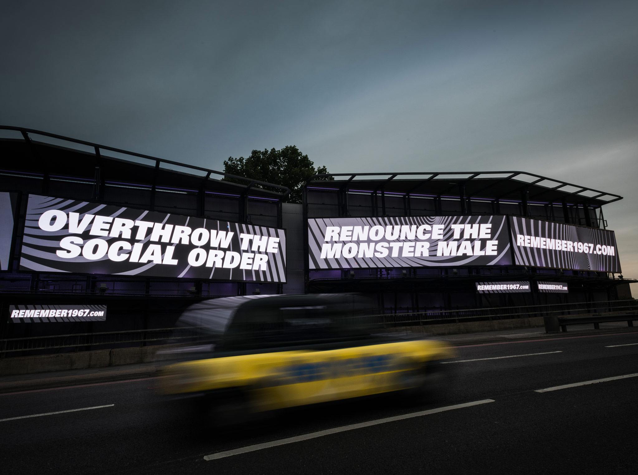 Bauer Media Outdoor Storm Cromination featuring a REMEMBER1967 campaign, on a busy roadside as a yellow taxi passes by.