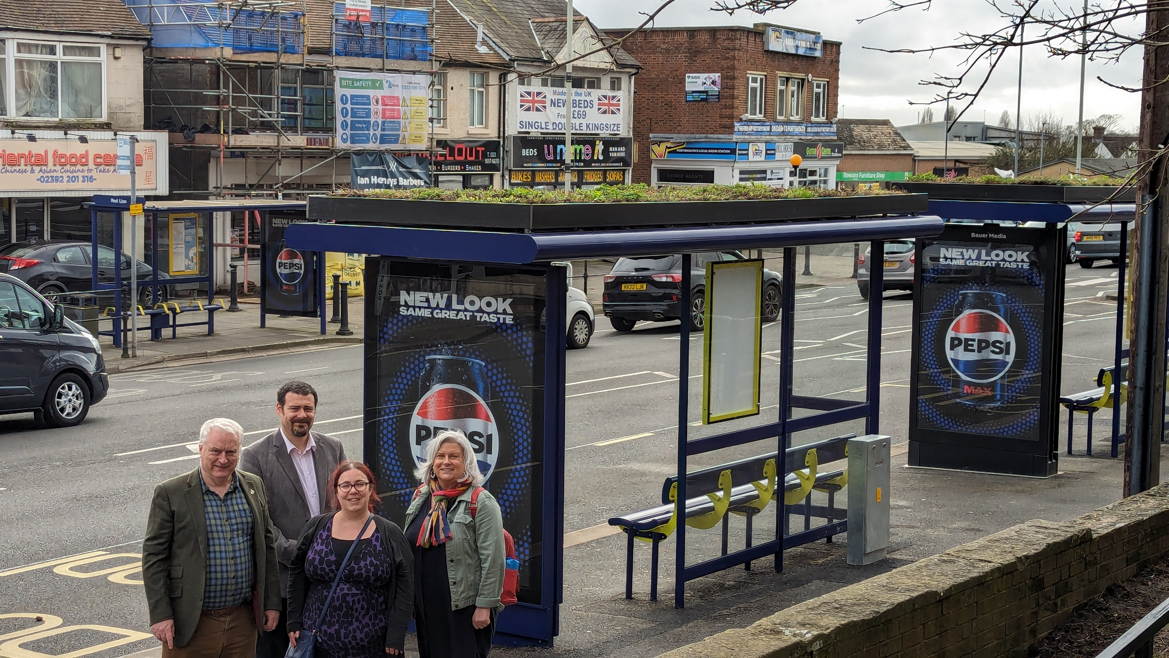 Bauer Media Outdoor UK and Portsmouth representatives standing beside a Living Roof bus shelter on a busy street during the day