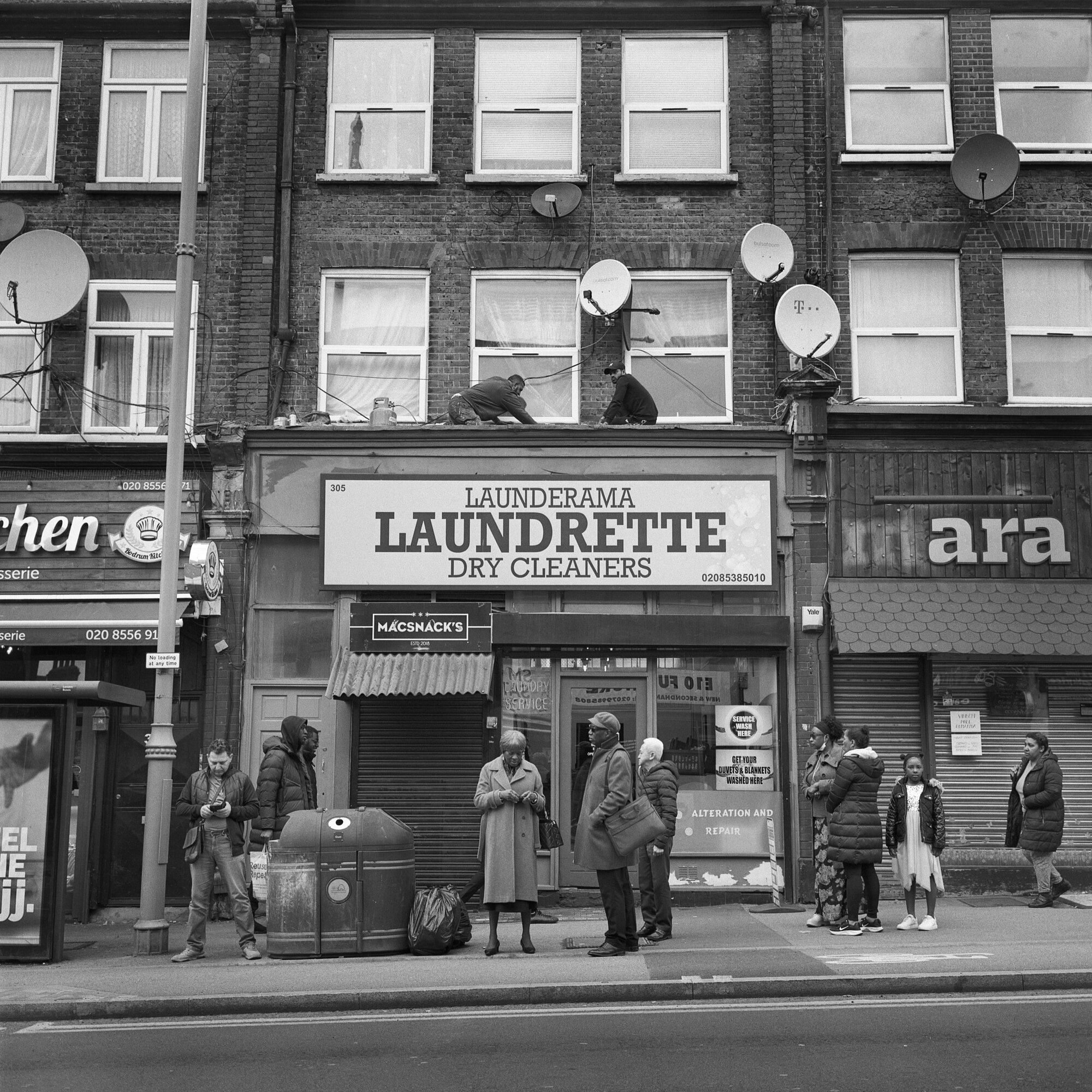 People standing outside a launderette waiting for a bus
