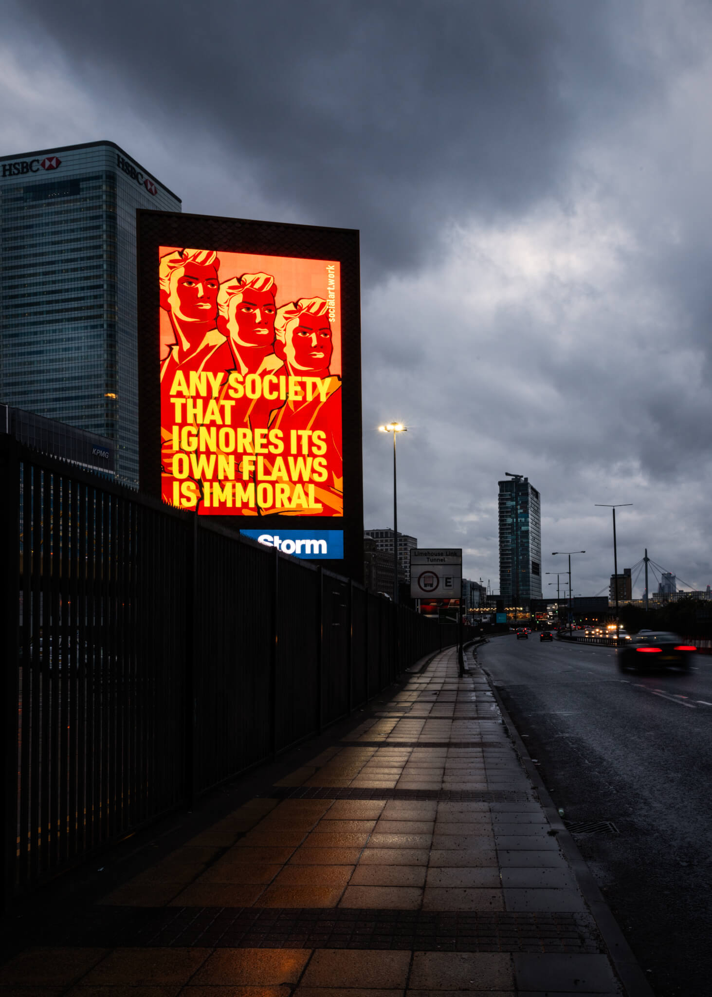 Storm billboard displaying Martin Firrell's artwork for a fairer society by a busy roadway