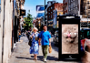 A Bauer Media Outdoor digital screen displaying an Many Pets on a busy pedestrian street, with shoppers walking past on a sunny day.