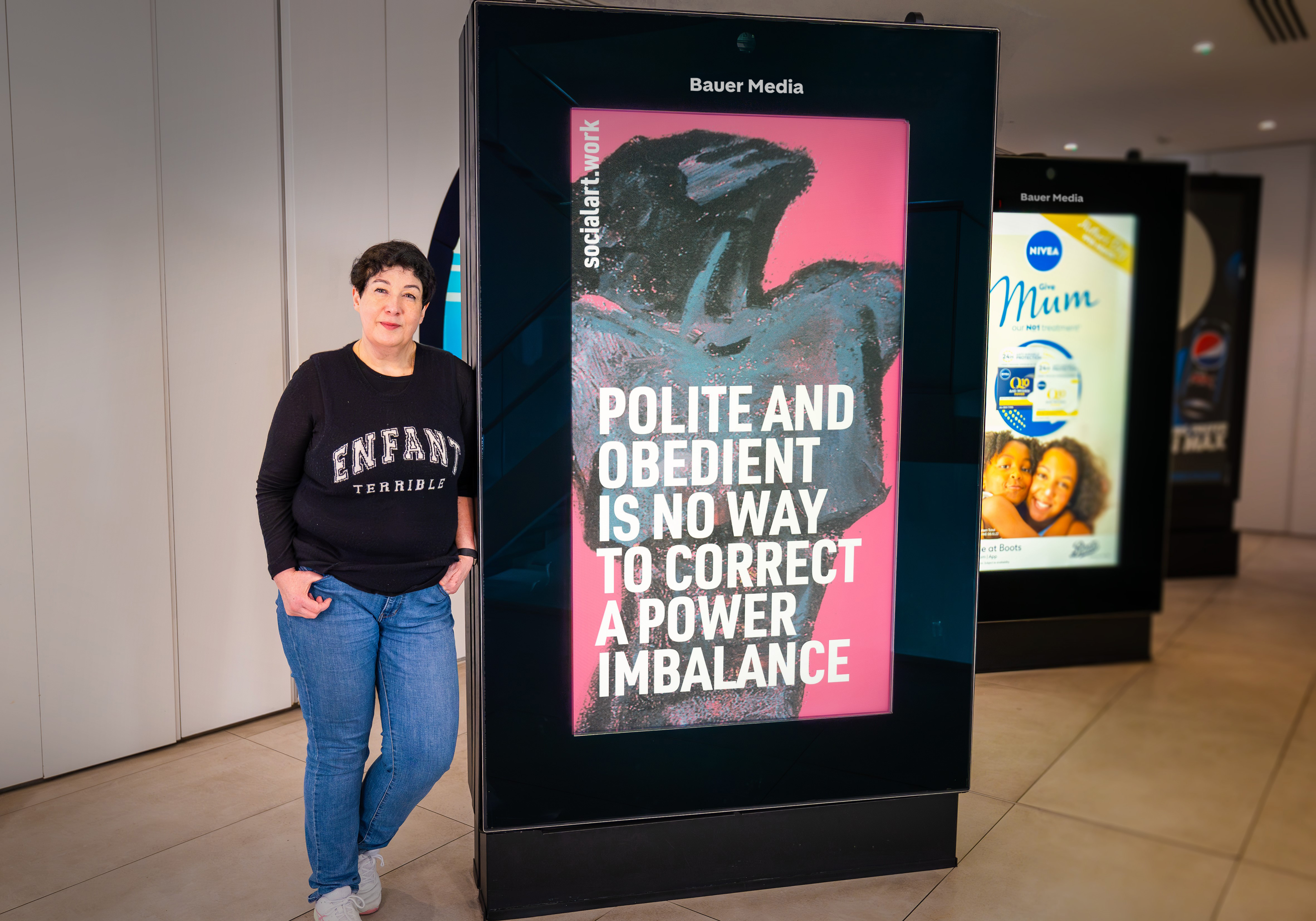 Joanne Harris, novelist, Chair Society of Authors, stands in front of a digital screen displaying her quote and artwork by Martin Firrell, at Bauer Media Outdoor's HQ in London