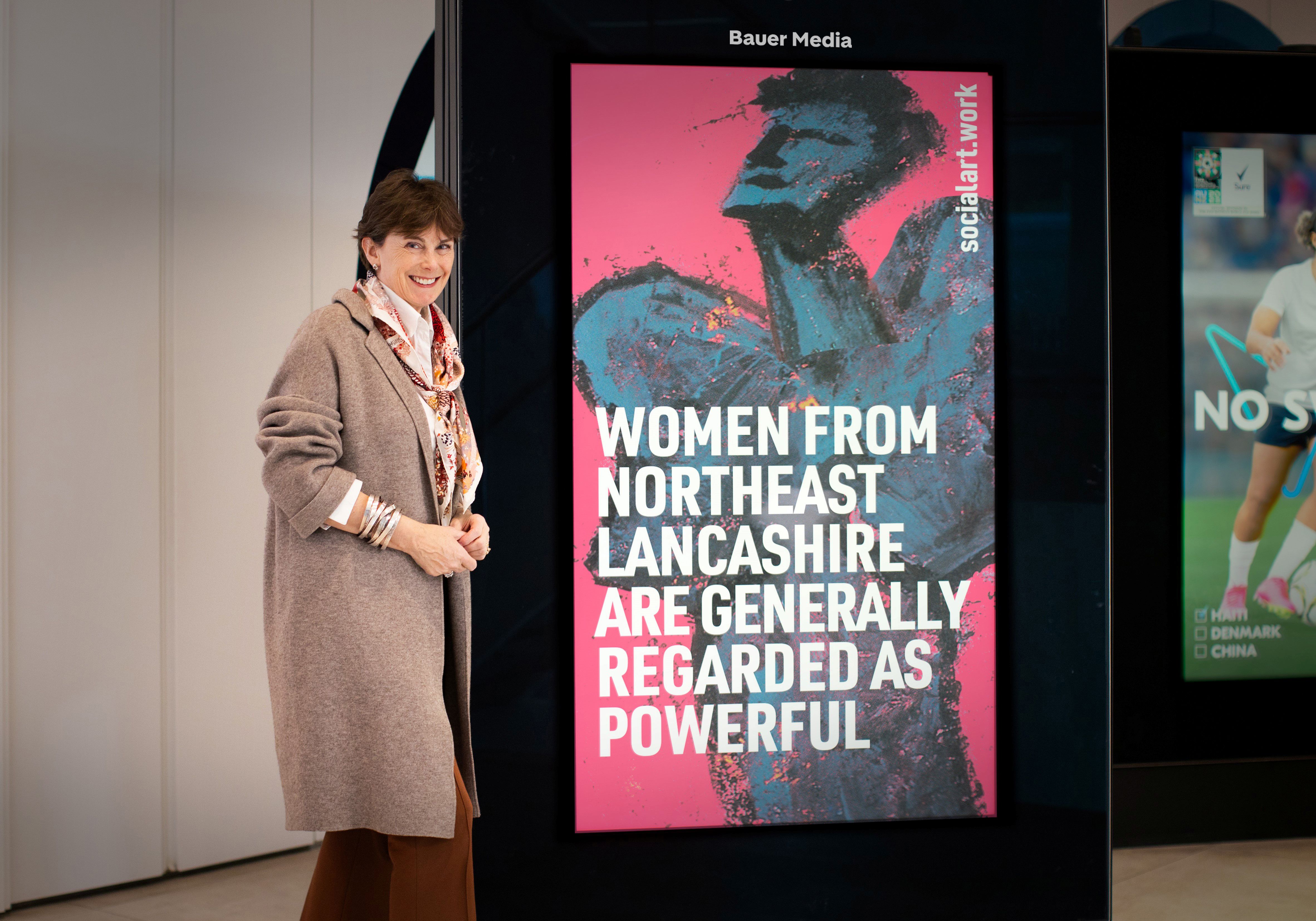 Heather Hancock, Master St. John’s College, Cambridge, stands in front of a digital screen displaying her quote and artwork by Martin Firrell, at Bauer Media Outdoor's HQ in London