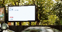 A British Airways roadside billboard with minimalist copy reading “Business. Leisure. Halloween in Transylvania,” seen beside trees with blurred traffic passing in front.