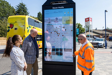 A Bauer Media Outdoor UK representative demonstrates using the new wayfinder unit installed outside Solihull Station, during the day, as local council representatives watch.