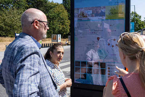 Members of Solihull Council and a local resident explore a new wayfinder unit, installed outside Solihull Station, during the day.