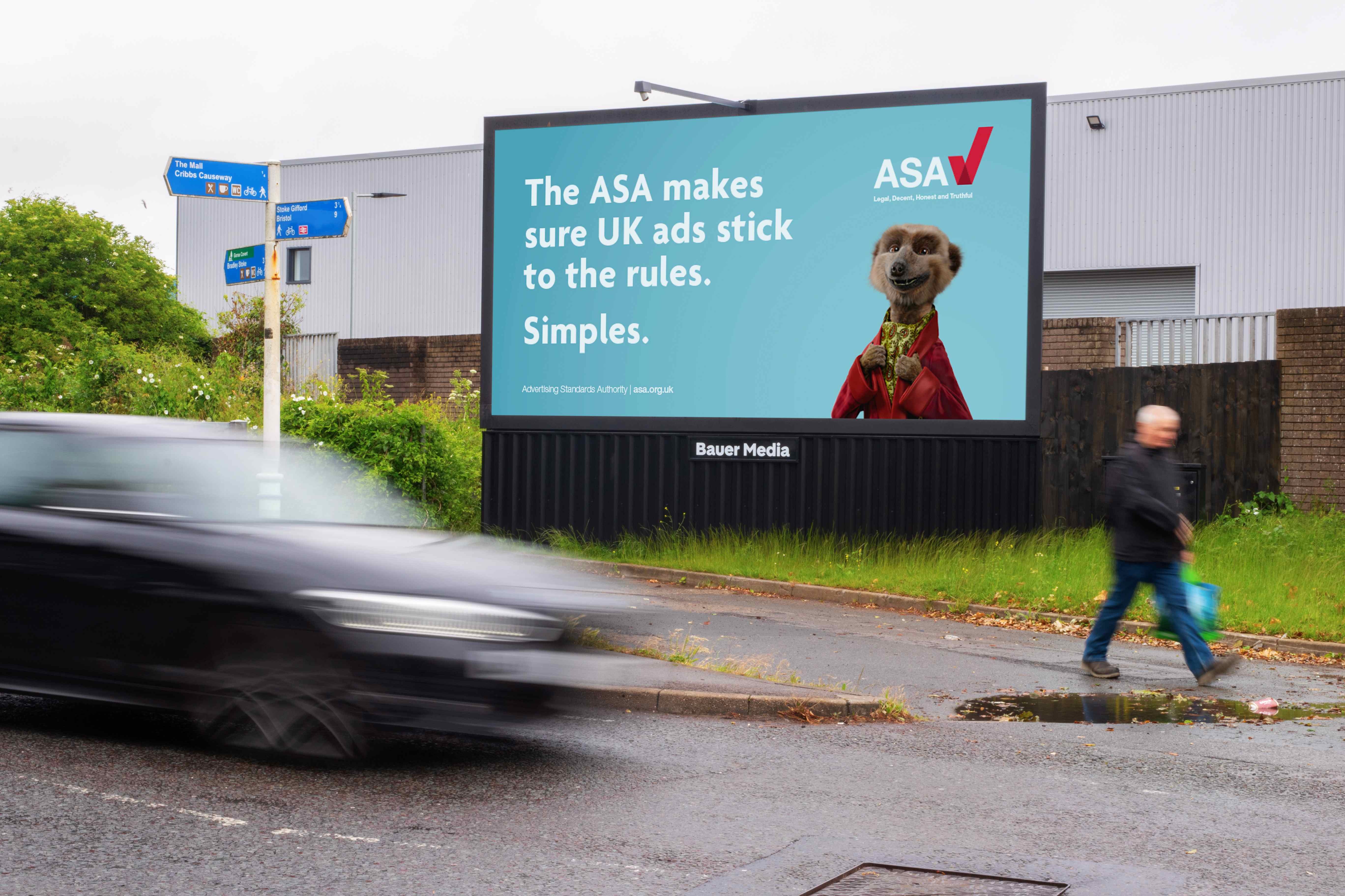 Bauer Media Outdoor billboard displays an ASA advert with the text: “The ASA makes sure UK ads stick to the rules. Simples.” The ASA logo appears alongside a meerkat character on a turquoise background, with traffic and pedestrians passing in the foreground.