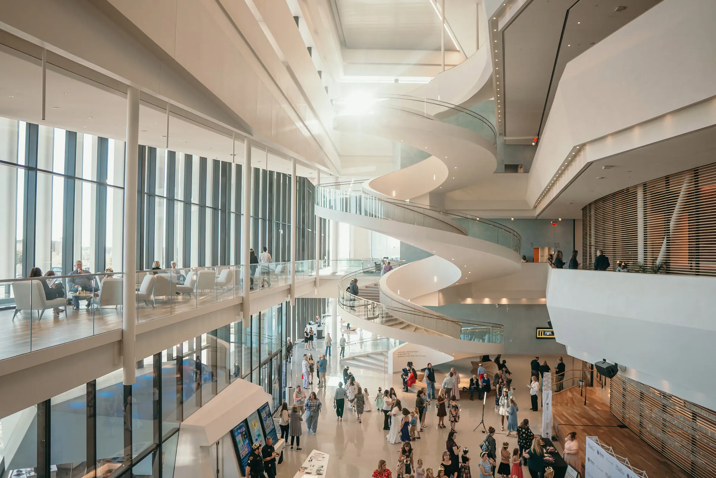 Crowd gathered in a bright modern lobby with a sculptural spiral staircase.