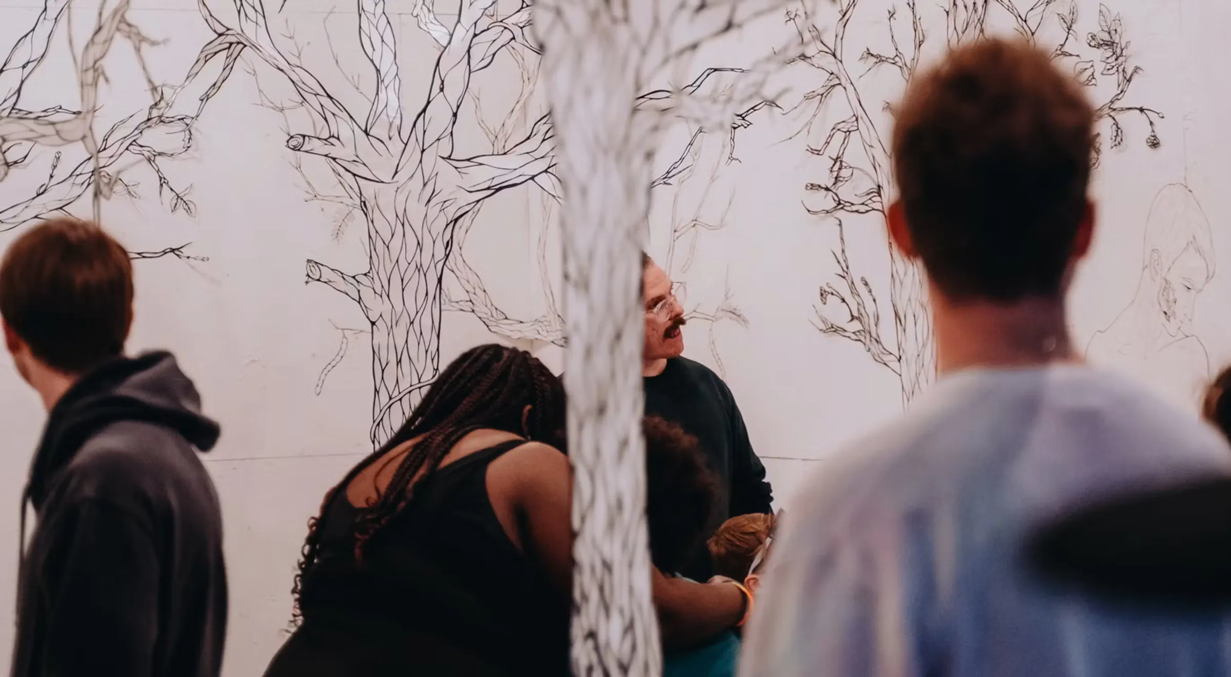 People conversing in front of a tree-mural wall at an event.