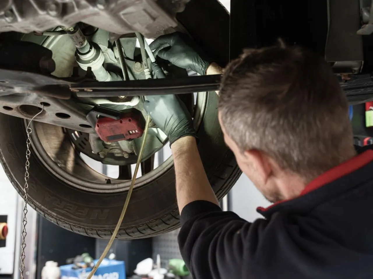 Mechanic wearing black gloves inspecting the underside of a car near the rear tire.