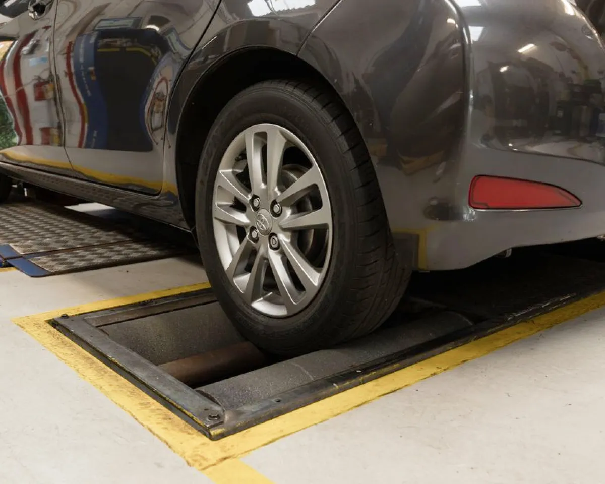 Close-up of a car's rear wheel on a vehicle inspection roller in a garage.