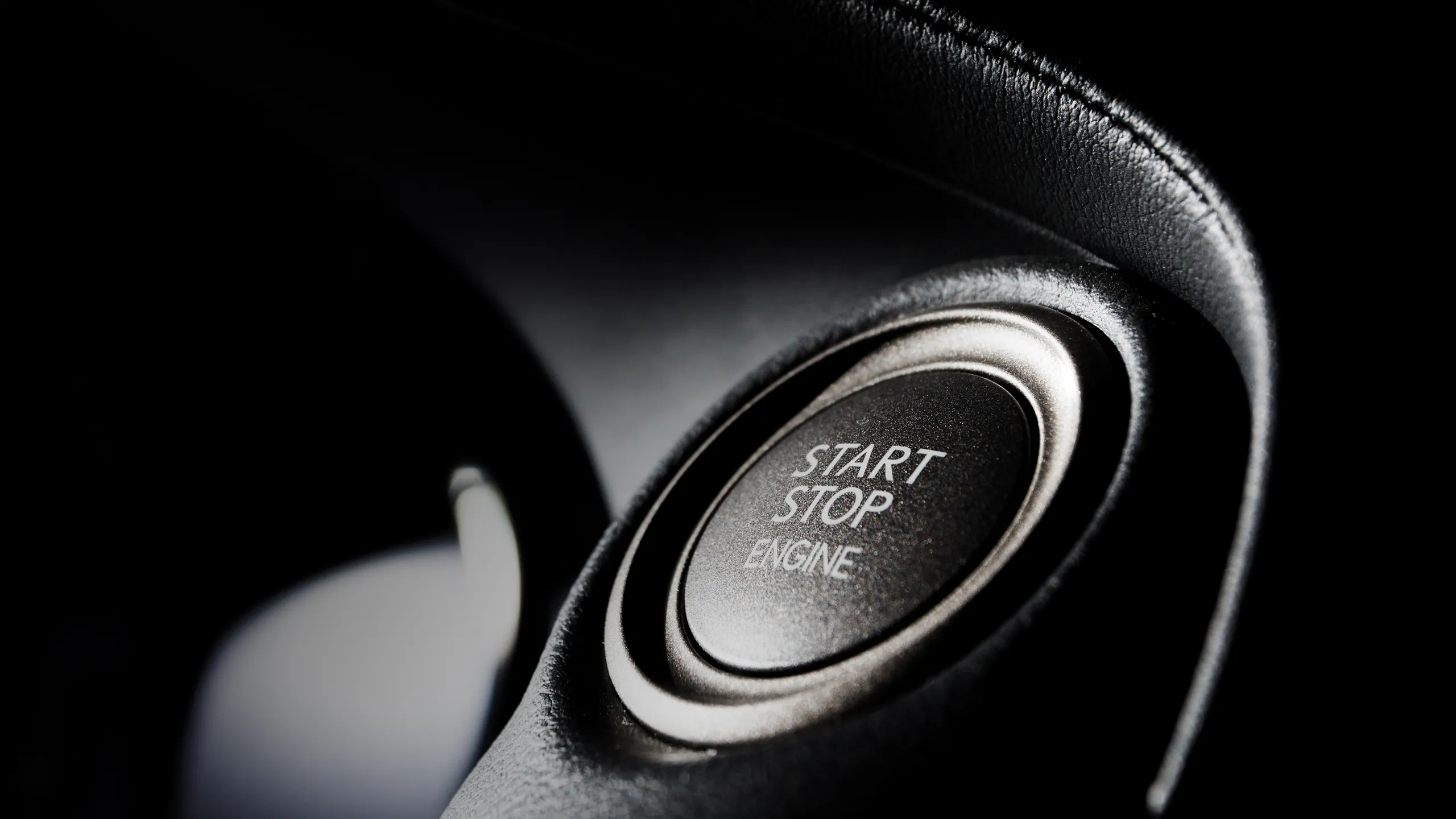 Close-up of a car's start-stop engine button surrounded by textured black dashboard material.