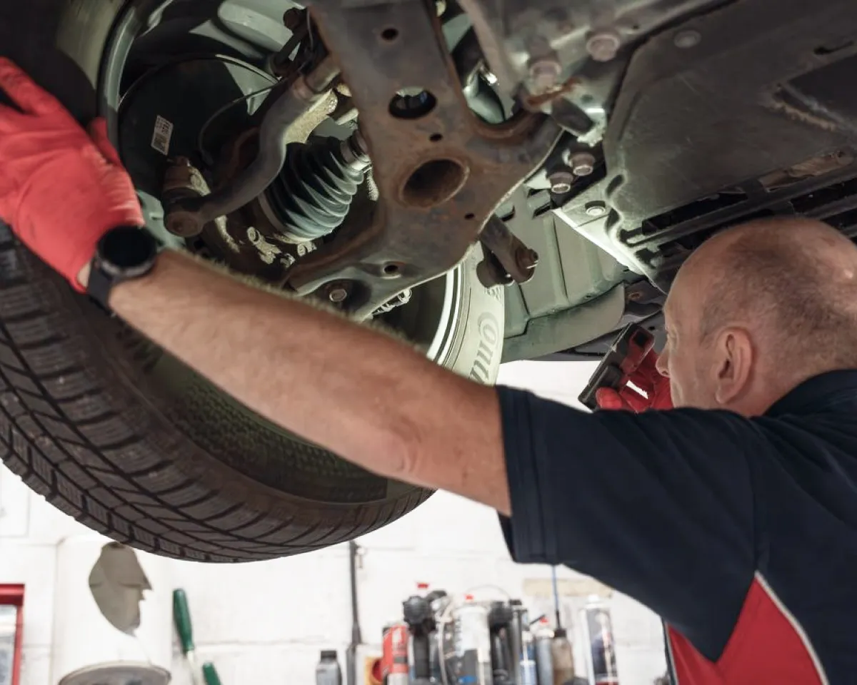 Mechanic wearing red gloves inspecting the underside and tire of a raised vehicle.