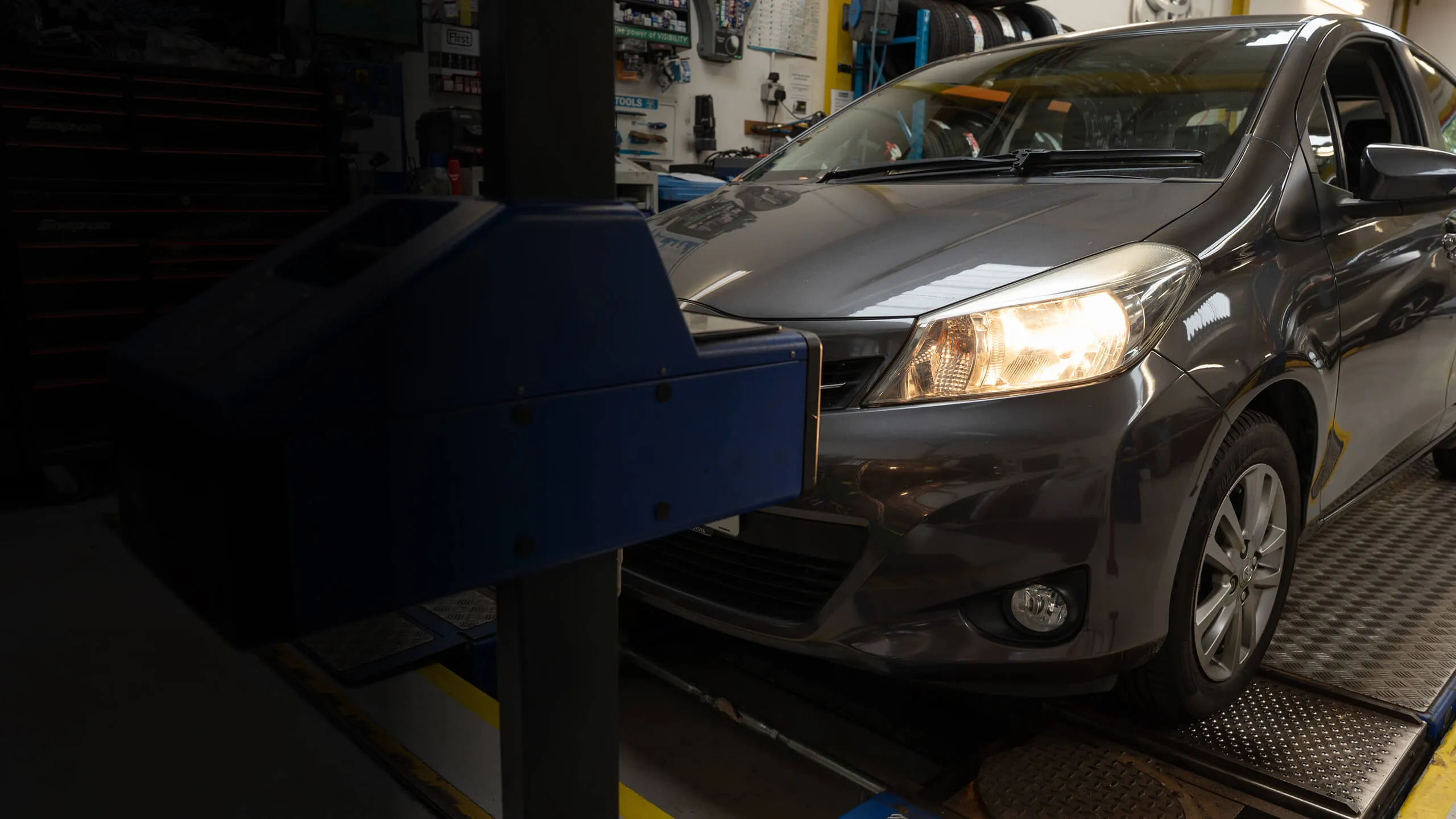 Gray car with headlights on positioned on a vehicle inspection platform in a garage.