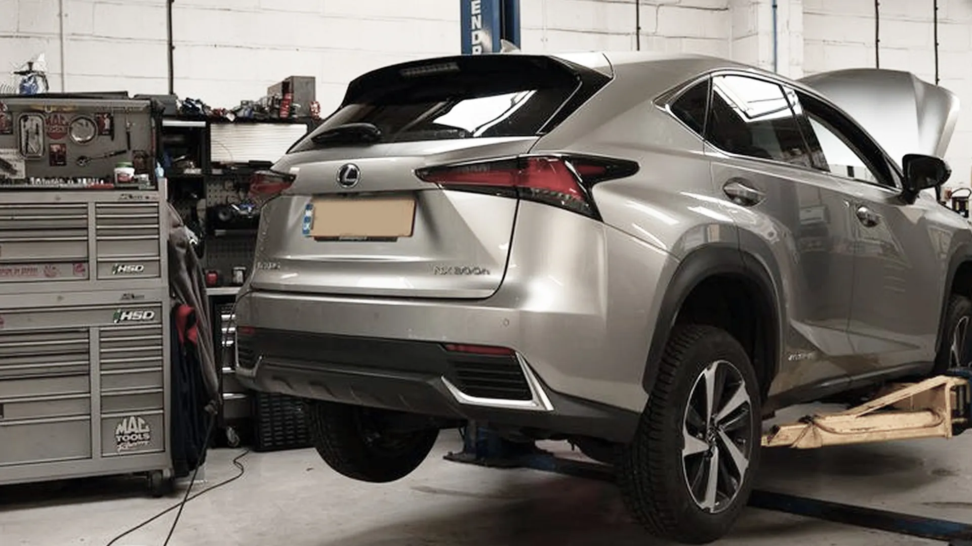 Silver Lexus NX 300h SUV raised on a hydraulic lift in a garage workshop with its hood open.
