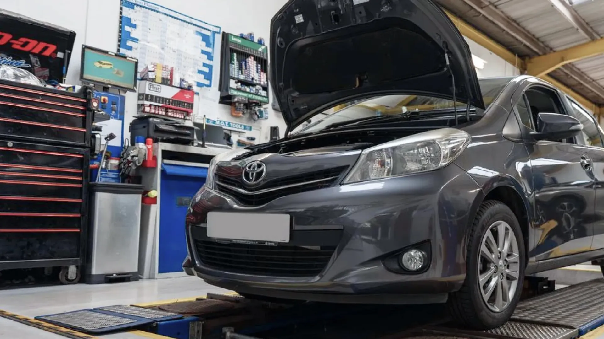 Gray Toyota car with open hood inside an auto repair shop near a tool cabinet.