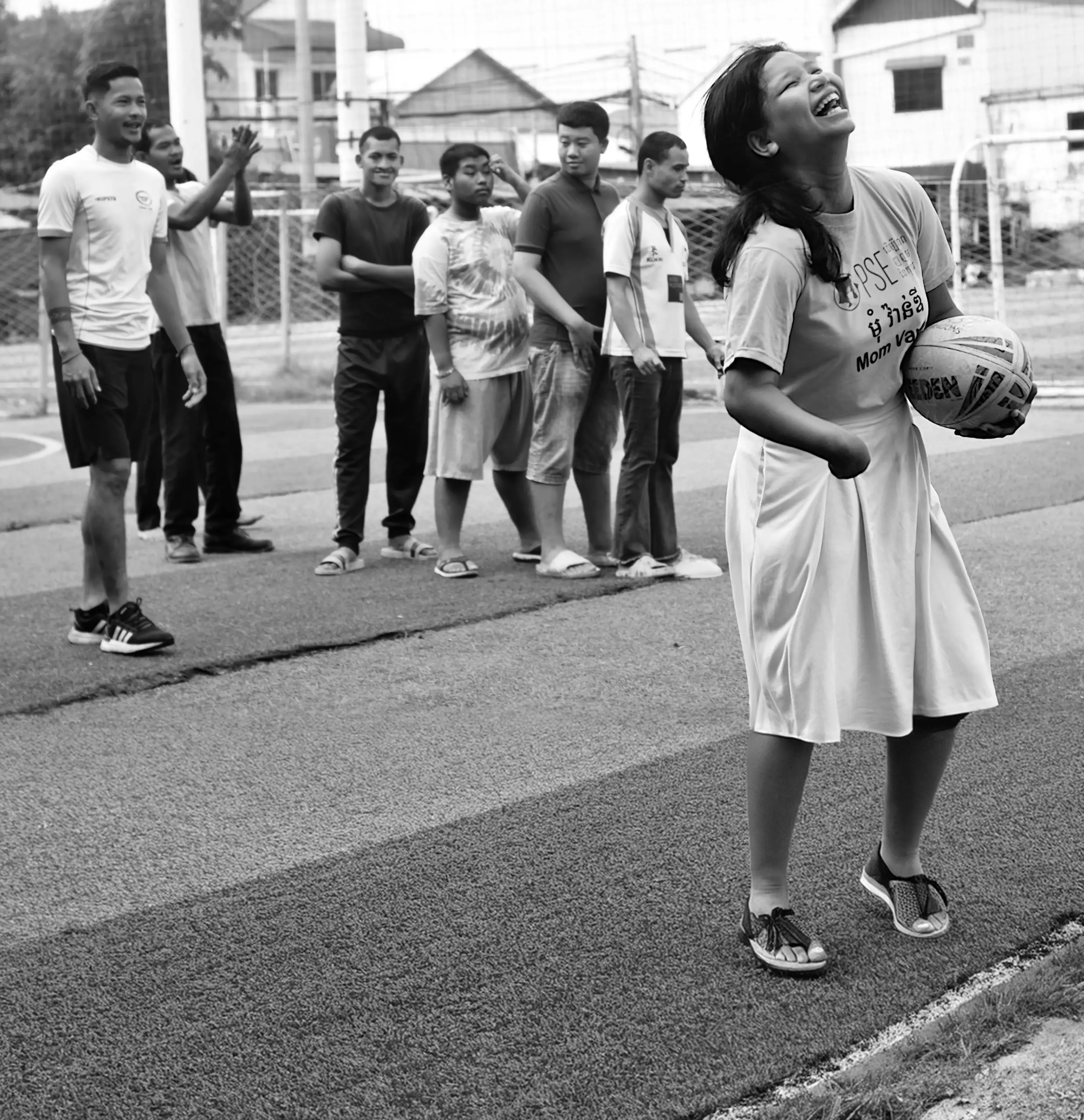 A young girl with a physical disability smiling and holding a rugby ball. 5 boys standing up at the back.