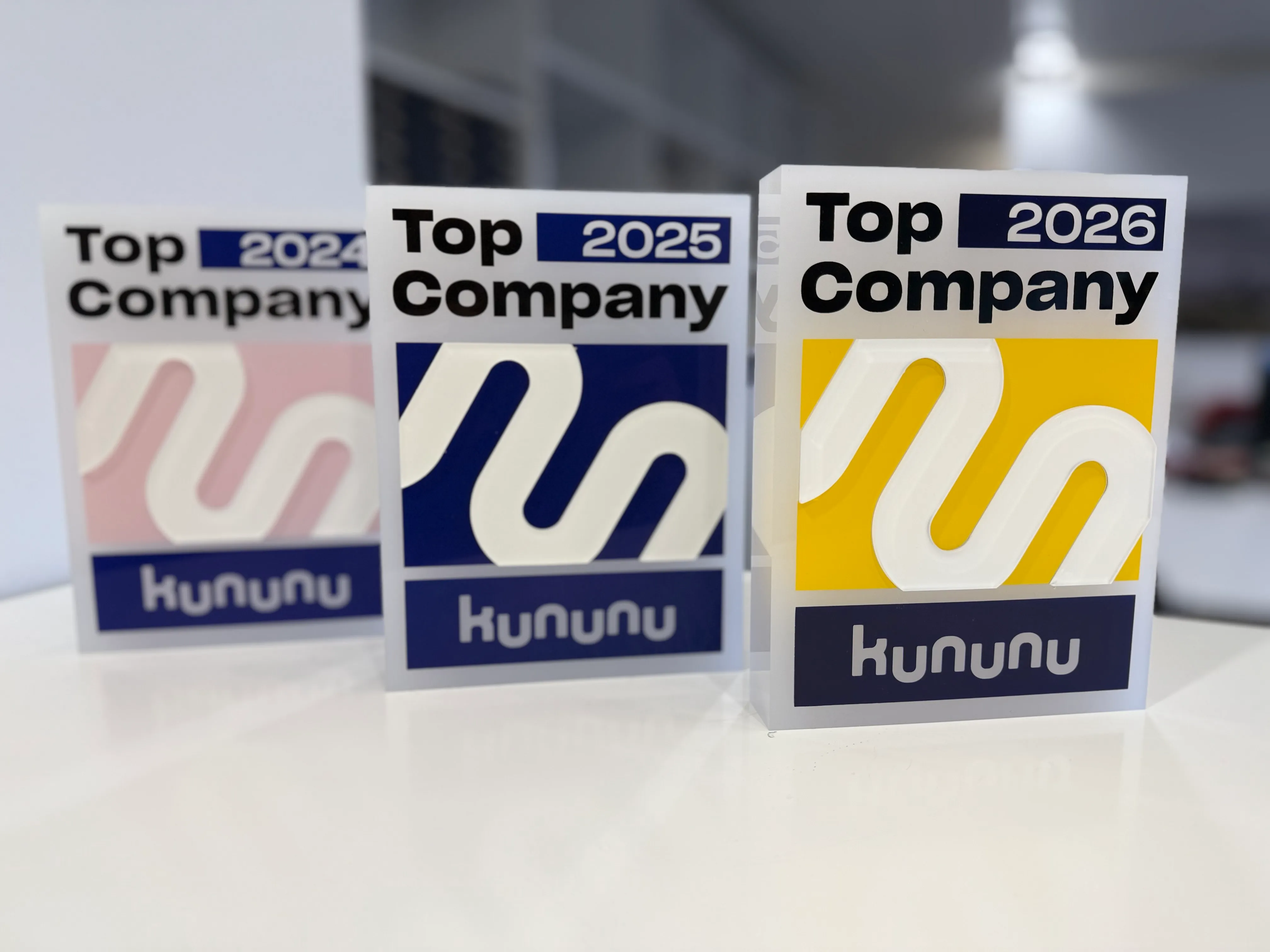 Kununu Auszeichnungen für Top-Unternehmen der Jahre 2024, 2025 und 2026 auf einem weißen Tisch.