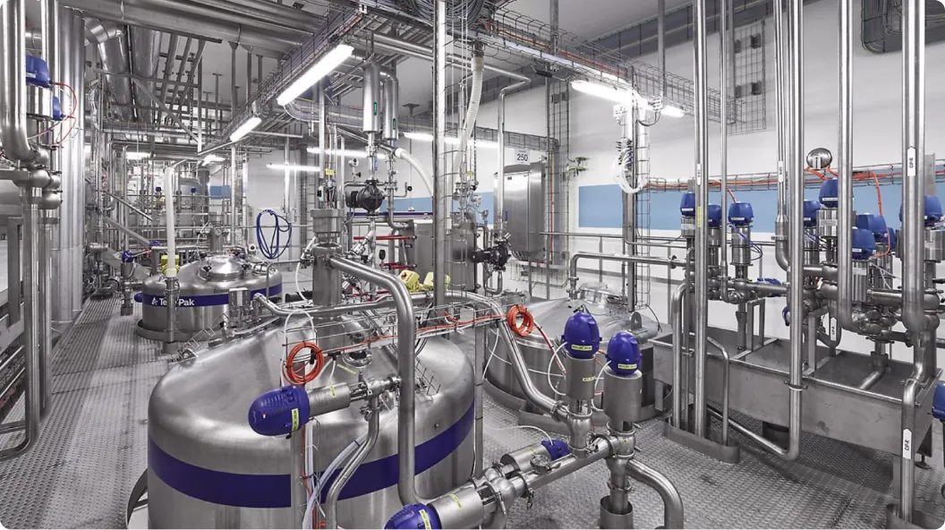 Industrieller Produktionsraum mit zahlreichen Edelstahlrohren, Tanks und Ventilen in einer sauberen, hell beleuchteten Anlage.