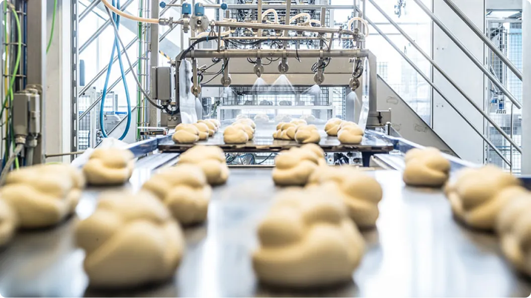 Teiglinge werden auf einem Förderband in einer Bäckerei-Maschine automatisch besprüht.