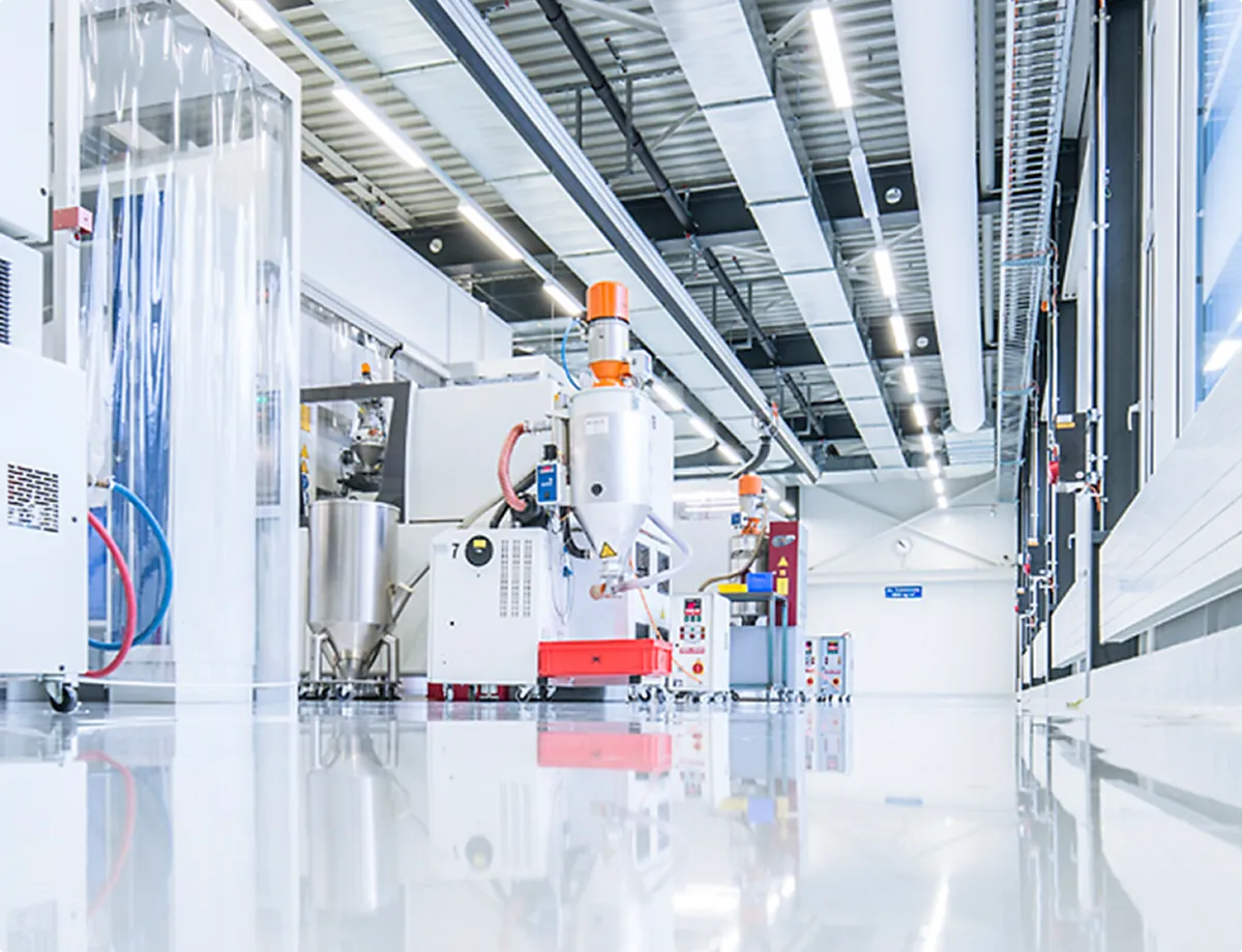 Industrial building with white, reflective floor and modern production machine with orange components.