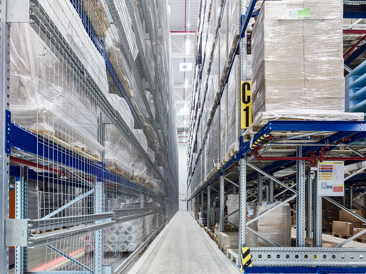 Hochregallager mit dicht befüllten Palettenregalen und schmalem Gang für effiziente Lagerung und Logistikprozesse.