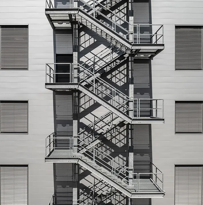 Eine Außenfassade mit zentraler Außentreppe eines mehrstöckigen Industriegebäudes, die die Flächeneffizienz und vertikale Struktur moderner Fabrikkonzepte verdeutlicht.