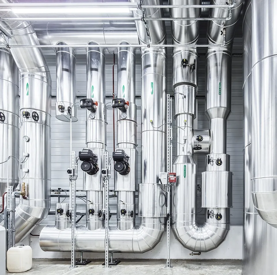 Moderne Gebäudetechnik mit isolierten Rohrleitungen und Heizungs‑ bzw. Lüftungsanlagen in einem technischen Betriebsraum.