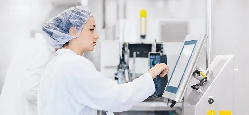 An employee wearing full cleanroom clothing operates a technical device in a high-purity, GMP‑compliant clean room