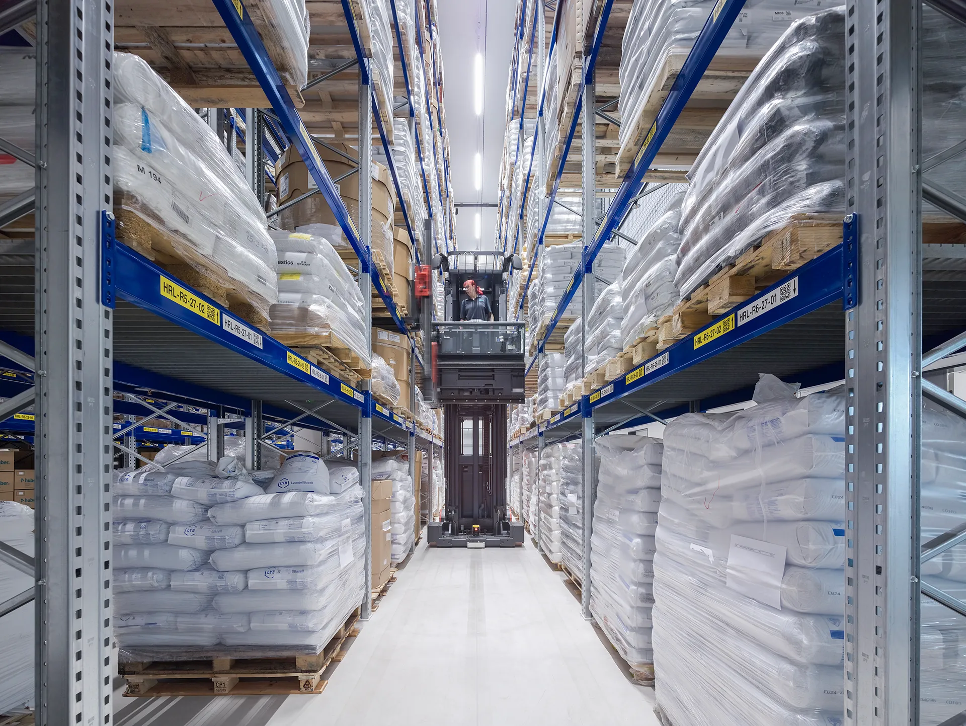 Ein Hochregallager mit gestapelten Paletten und einem automatisierten Gabelstapler, der Waren in einer sauber strukturierten Logistikhalle bewegt.