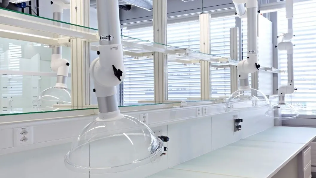 Laborarbeitsplatz mit weißen Abluftanlagen und großen Fenstern mit Jalousien im Hintergrund.