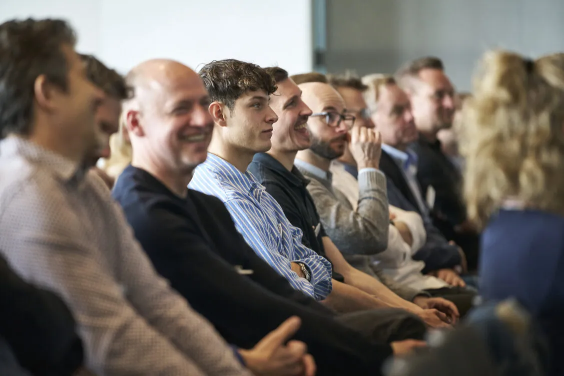 Menschen sitzen in einer Reihe und hören aufmerksam bei einer Veranstaltung zu.