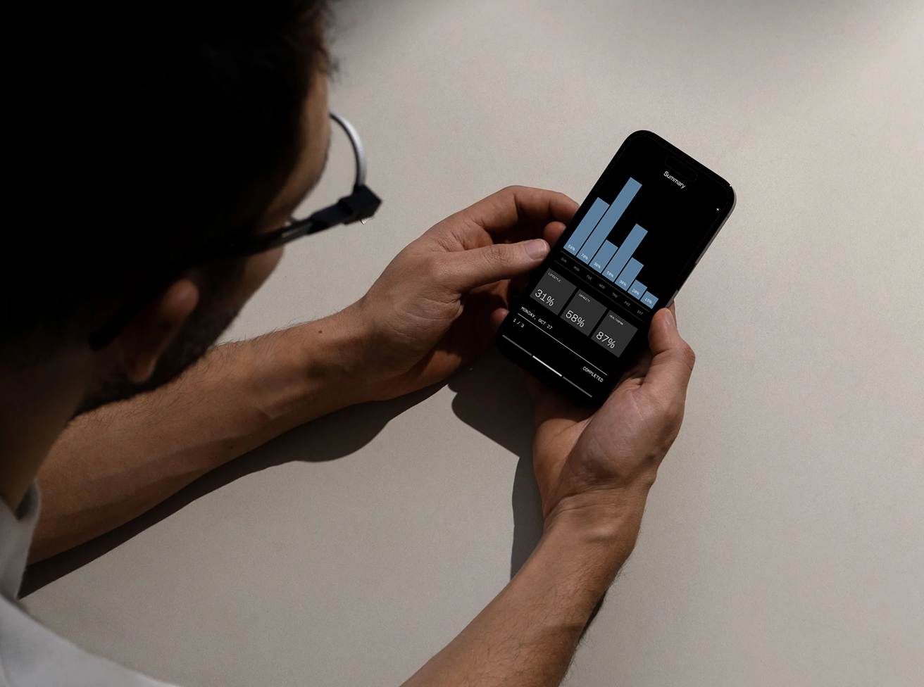 Person wearing glasses holding a smartphone displaying a summary bar chart with percentages and data metrics.