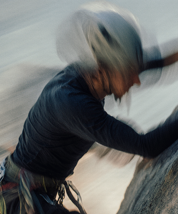 Person wearing a helmet and climbing gear scaling a rock face in motion blur.