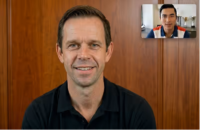 Man in black shirt smiling at camera with another man visible on video call in top right corner.