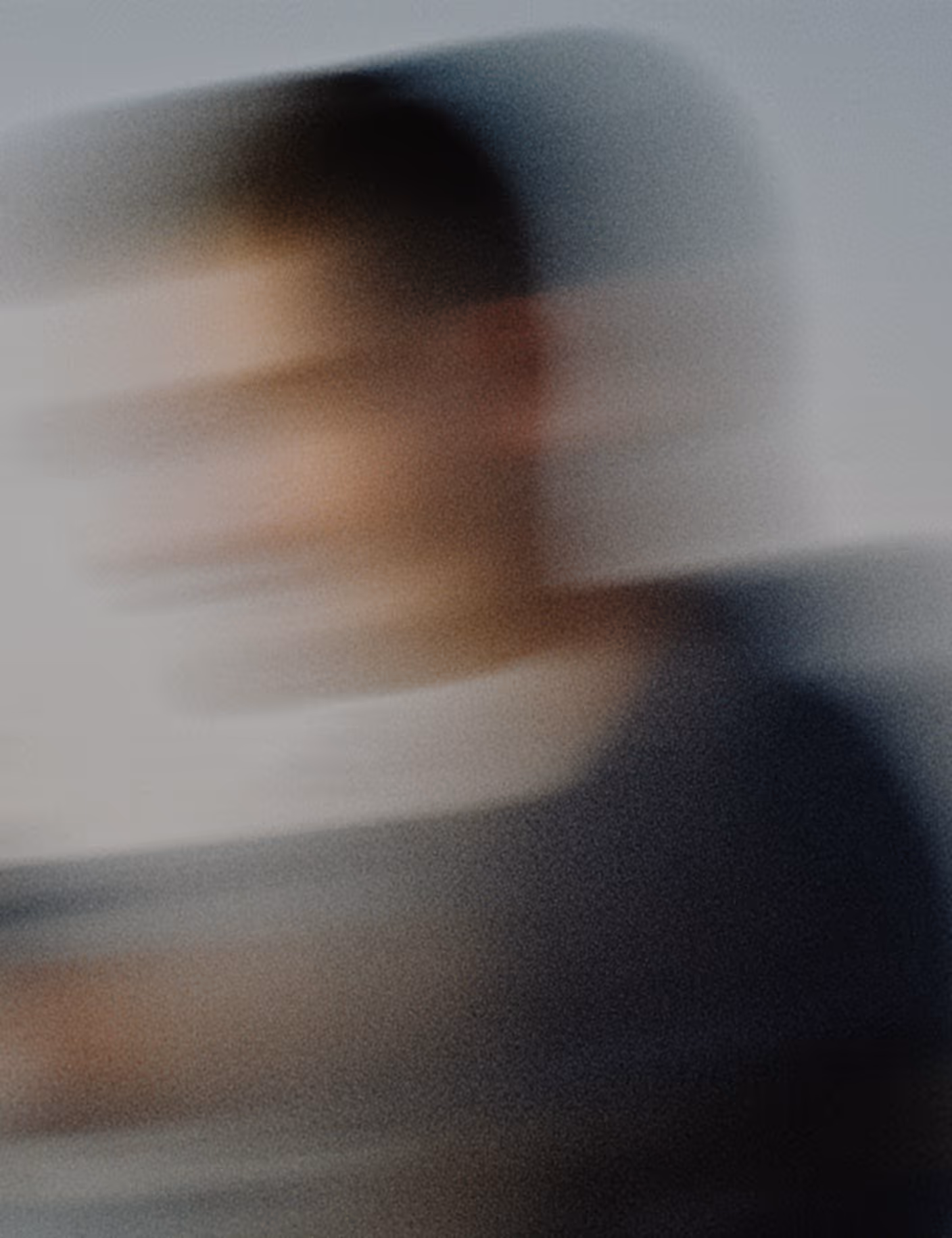 Blurred side profile of a person wearing dark clothing against a neutral background.
