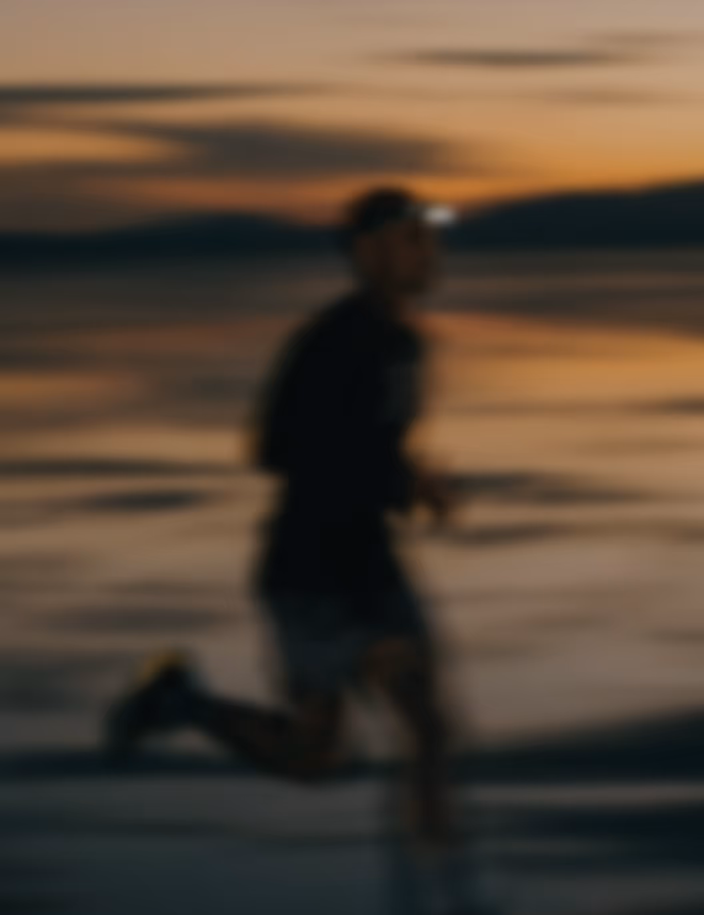 Person running on a beach at sunset with a blurred background.
