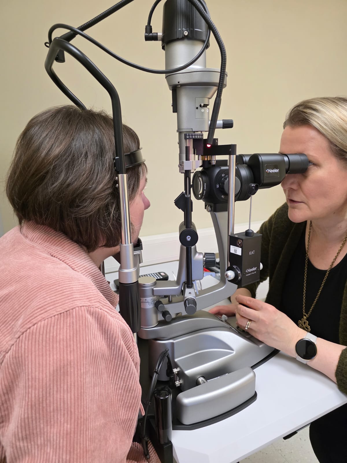An eye care professional examining a patient's eye using a slit lamp biomicroscope in a clinical setting.
