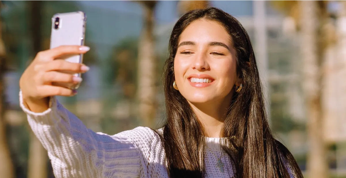 Woman looking at her smartphone taking an Identity Proof with Facial Recognition as a step in the identity verification process.