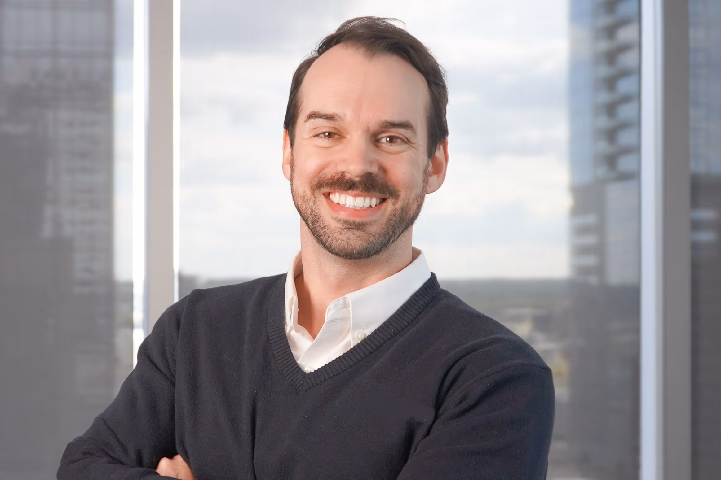 Portrait of Sean Jones standing with arms crossed in an office with large windows.