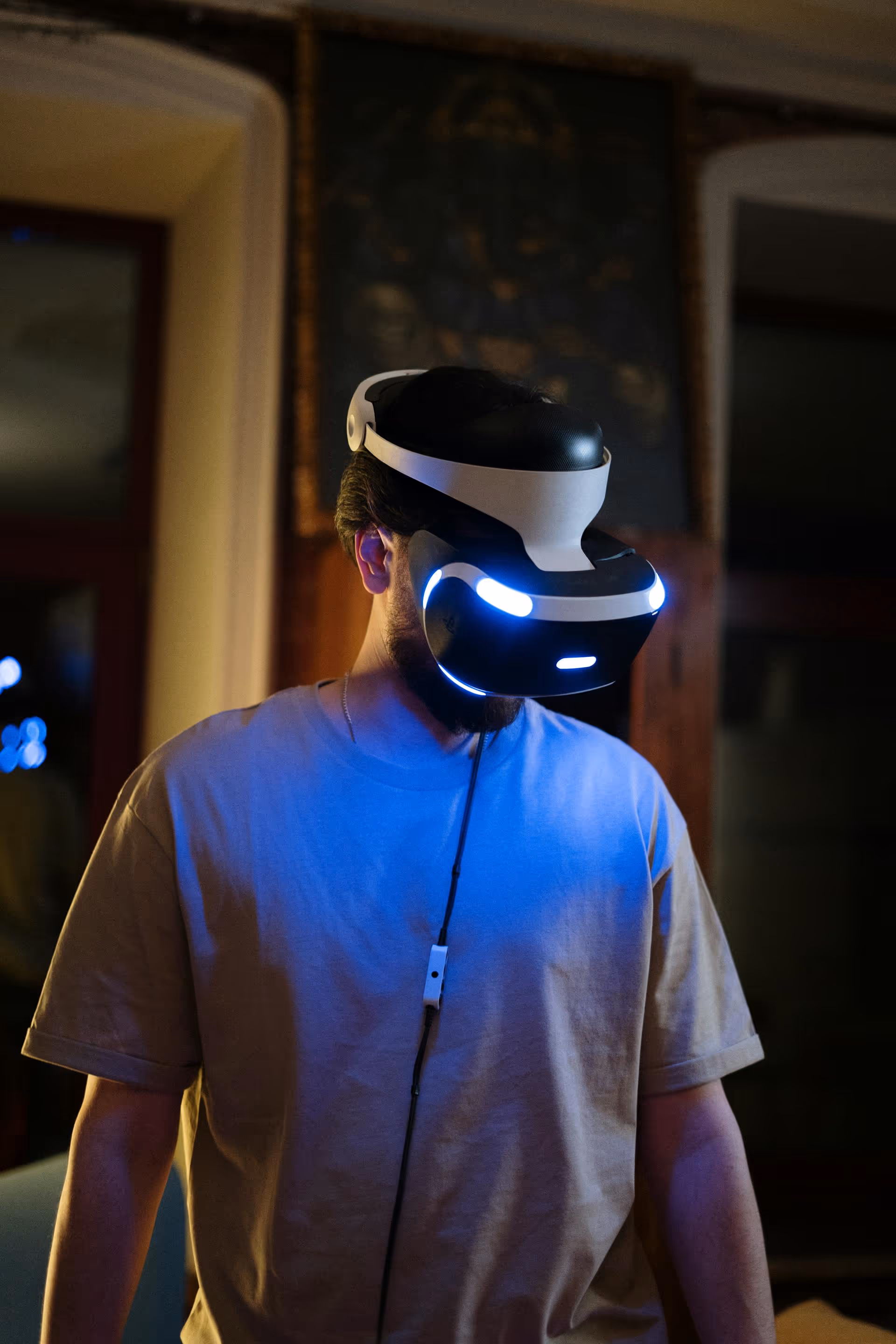 Man wearing a virtual reality headset with glowing blue lights in a dimly lit room.
