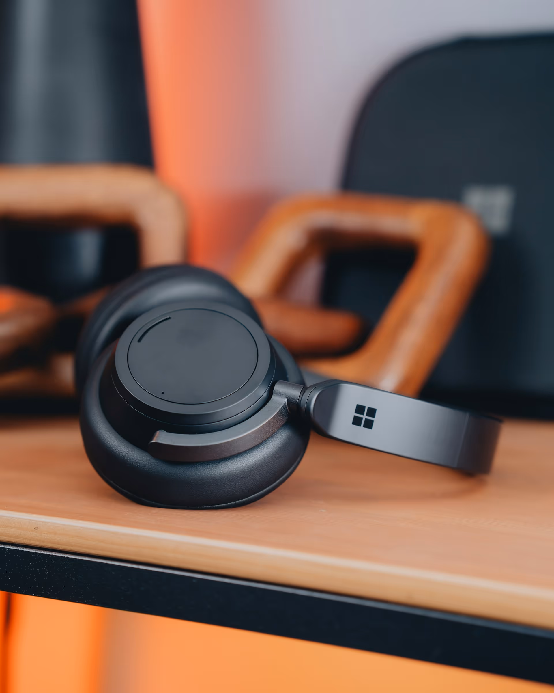 Black over-ear Microsoft headphones resting on a wooden desk with a blurred background.