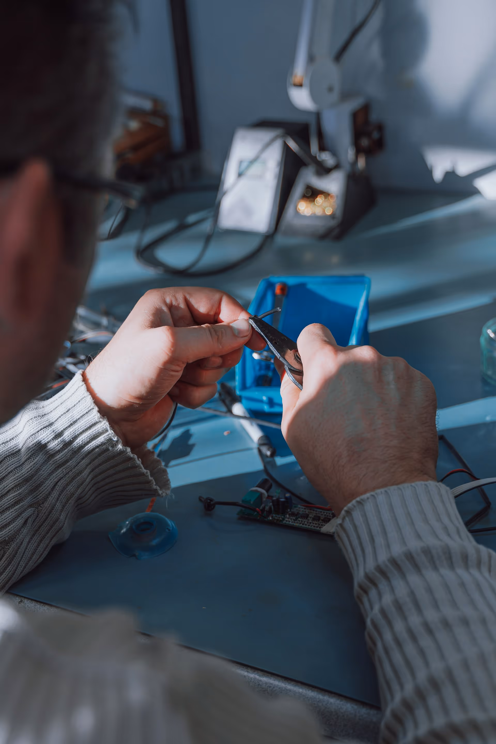 Person using pliers to work on a small electronic component at a workbench.