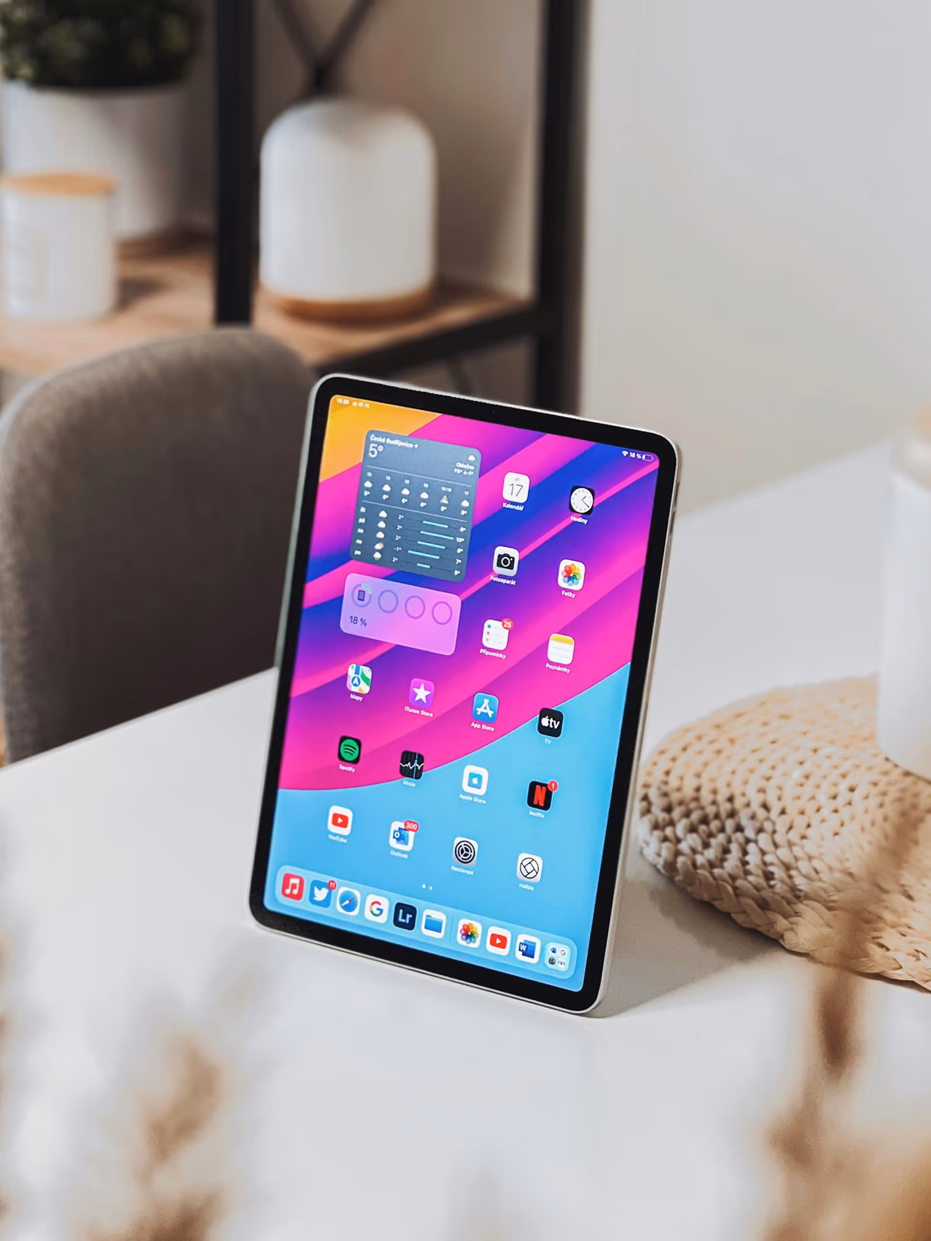 Tablet standing upright on a white table with colorful app icons on the screen in a cozy room setting.